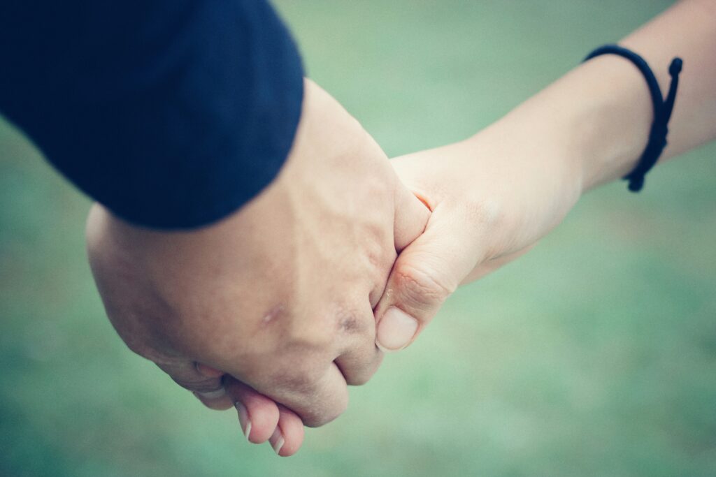 Duas pessoas de mãos dadas gentilmente, mostrando Cómo tener momentos de cariño y conexión cada día, fundo verde desfocado.