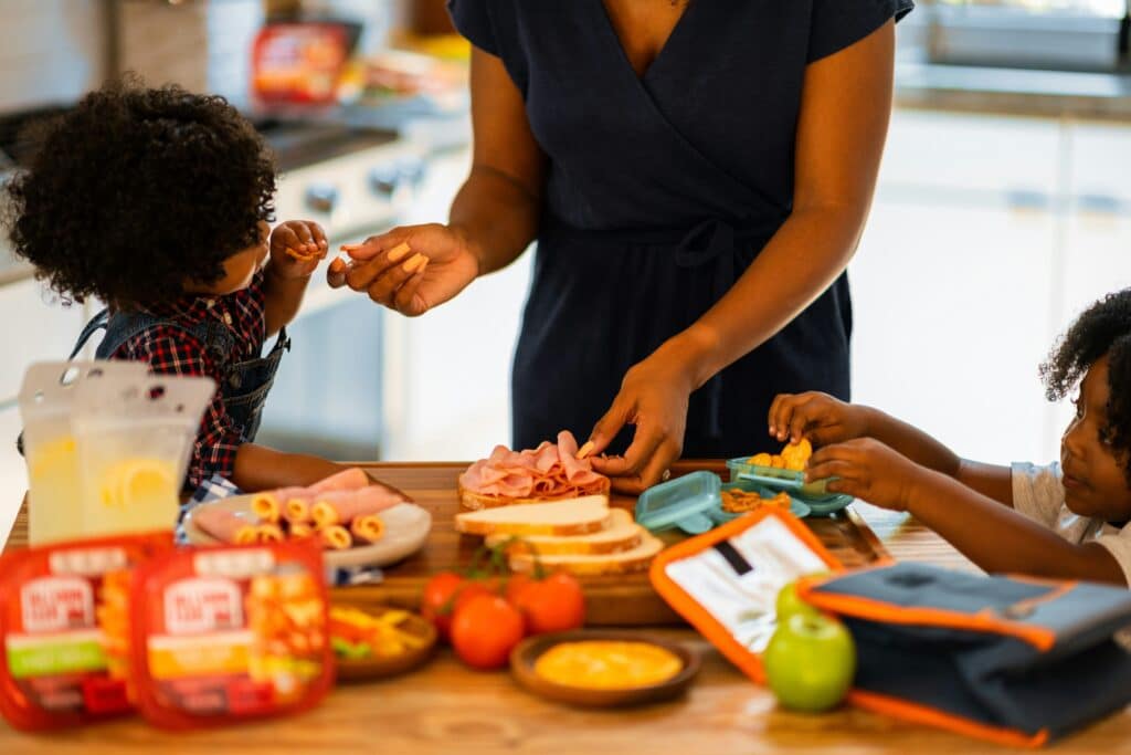 Ideas para hacer la hora de la comida más entretenida: um adulto e uma criança preparam sanduíches e lanches juntos na cozinha.